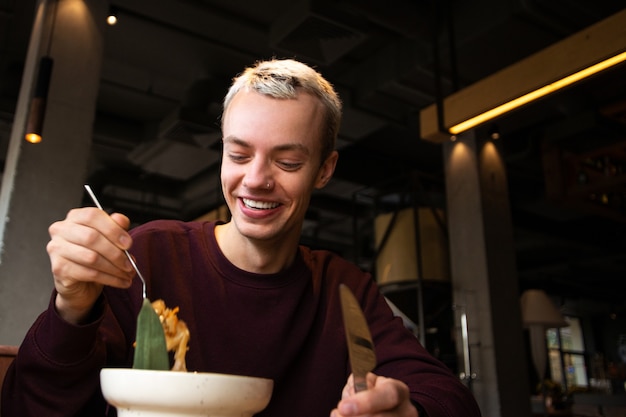 Happy young man smiles showing his teeth looking at tasty food on his fork