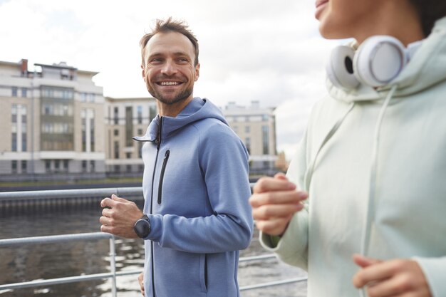 彼らが街で一緒にジョギングしている間彼のガールフレンドに微笑んで幸せな若い男