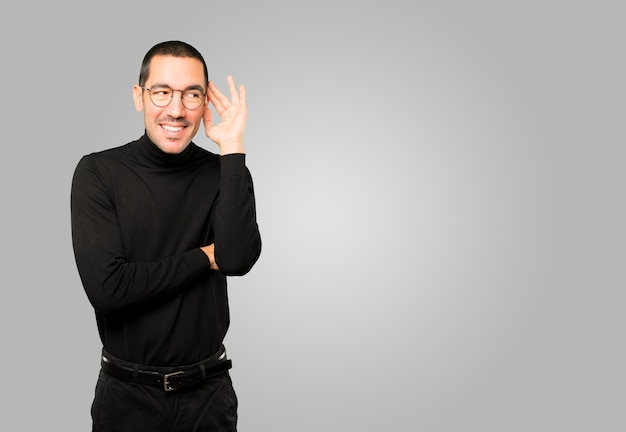 Happy young man smiling and making a gesture of trying to hear something