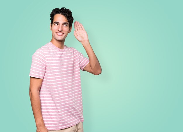 Happy young man smiling and making a gesture of trying to hear something