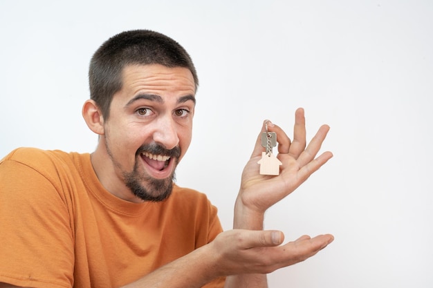 Happy young man smiling with the new home keys. Keychain in the shape of a wooden house.