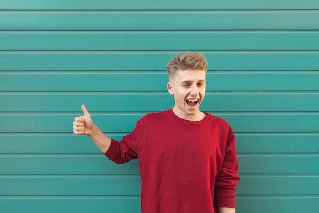 Happy young man standing on turquoise and showing a thumbs up.