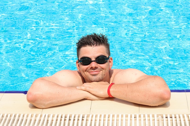 Happy young man swims in a turquoise pool. Smiling guy in swimming goggles.