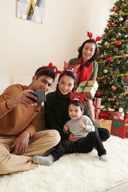 Happy young man taking selfie with wife son and motherinlaw at decorated christmas tree