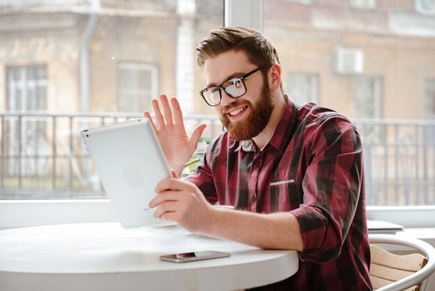 Happy young man talking with friends by tablet and waving.