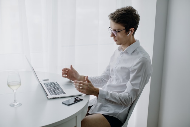 Photo happy young man, wearing glasses and smiling, as he works on his laptop. man in quarantine works at home. stay at home.