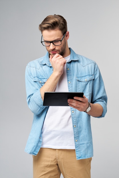 Happy young man wearing jeans shirt standing and using tablet