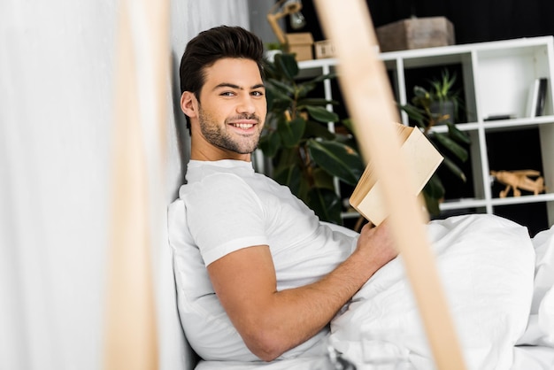 Happy young man with book in bed in the morning