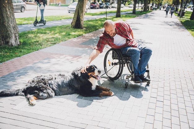 Счастливый молодой человек с ограниченными физическими возможностями в инвалидной коляске со своей собакой