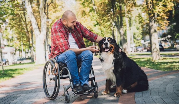 Счастливый молодой человек с физическими недостатками, который использует инвалидную коляску со своей собакой