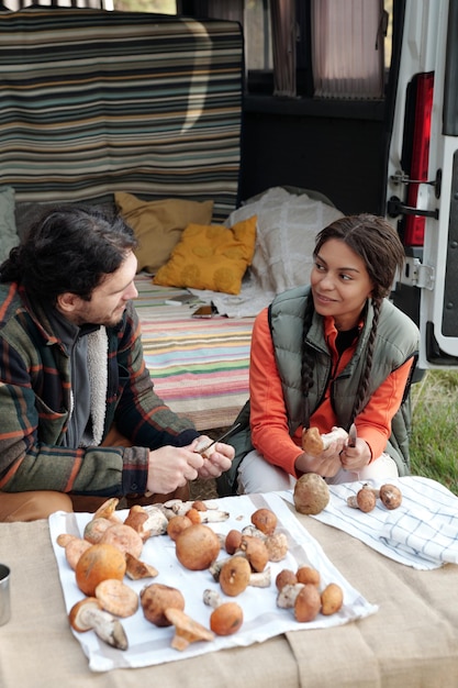 Happy young man and woman looking at one another while cutting porcini