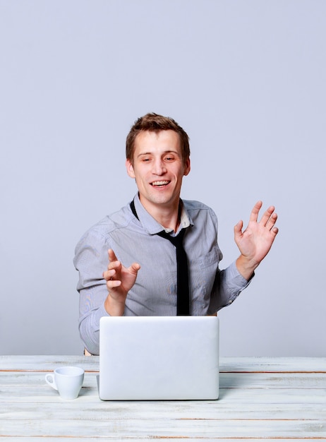 Happy young man working on laptop in the office on gray background