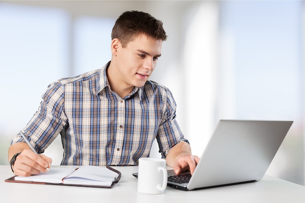 Happy young man works on his laptop with coffee at the table