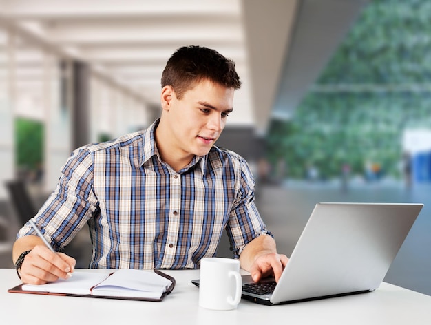 Happy young man works on his laptop with coffee at the table