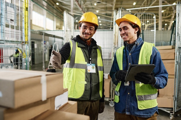 Photo happy young man in workwear using tablet and listening to colleague