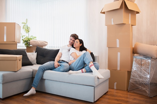 happy young married couple moves to new apartment. They are sitting on the sofa and looking at their new home.