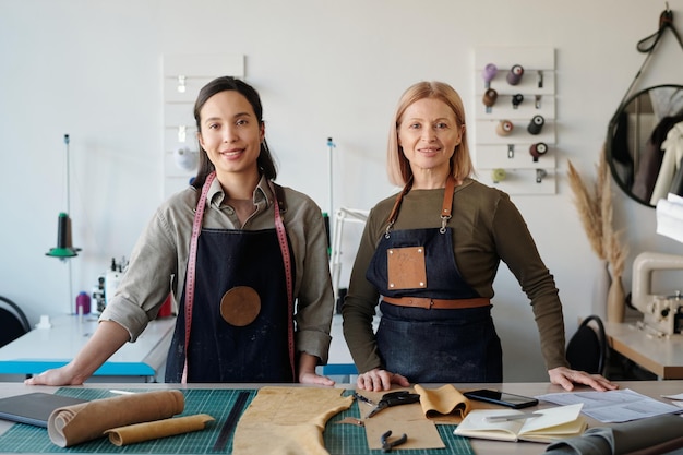 Happy young and mature craftswomen in workwear looking at camera