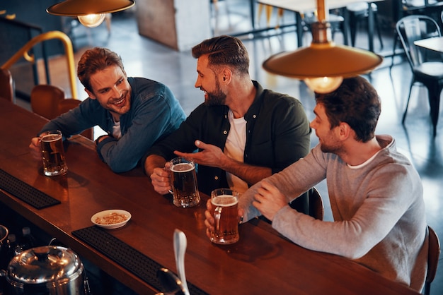 happy young men in casual clothing talking and enjoying beer