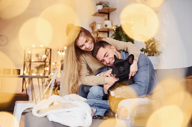 Happy young modern couple sitting on the sofa at home with their cute dog.