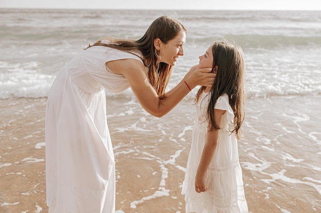 Happy young mom caressing cute daughter on sandy beach