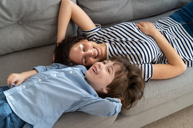 Happy young mom and little kid son relaxing on sofa at home