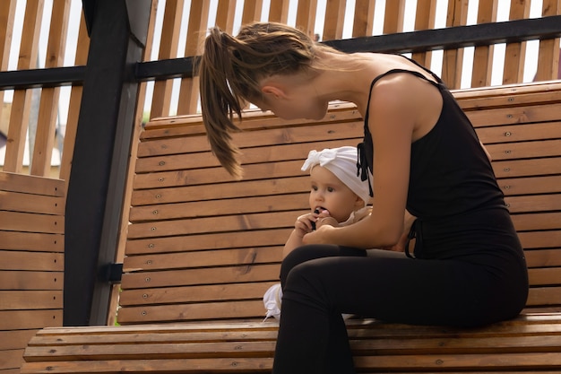 Happy young mom with her toddler daughter playing on a park bench