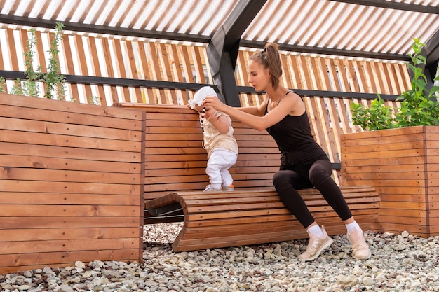 Happy young mom with her toddler daughter playing on a park bench