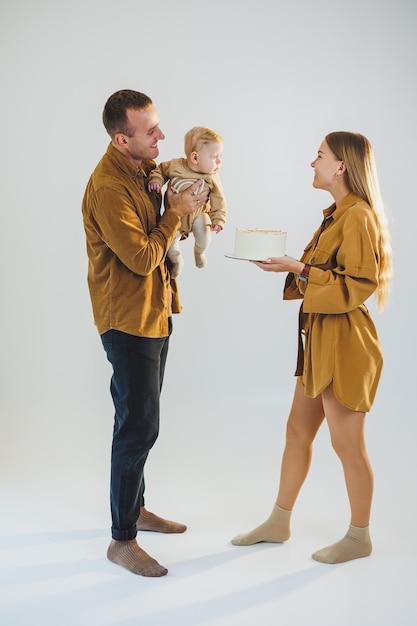 Happy young mother and father holding their newborn son in their arms and giving him a cake Parents celebrating their birthday with their little son The concept of family holidays