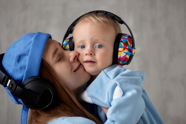 Happy young mother holds and hugs her smiling baby the baby and mom wear similar blue clothes and fu