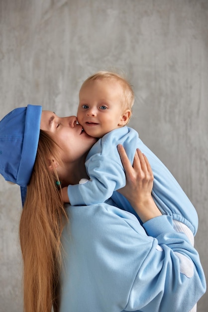 La giovane madre felice abbraccia il suo bambino sorridente e lo bacia il bambino e la madre indossano un vestito blu simile