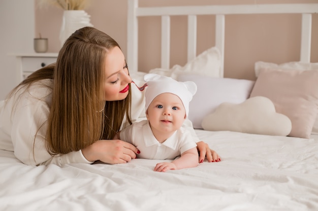 幸せな若い母親は自宅のベッドで幼児を抱擁します。