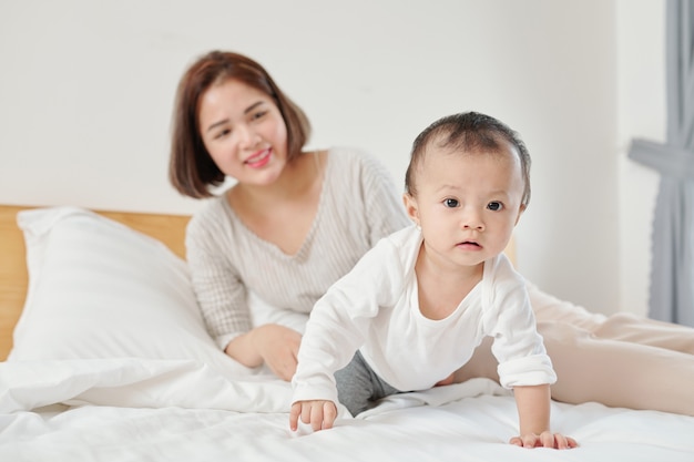 사진 침대에 크롤링 그녀의 사랑스러운 작은 아기를보고 행복 젊은 어머니