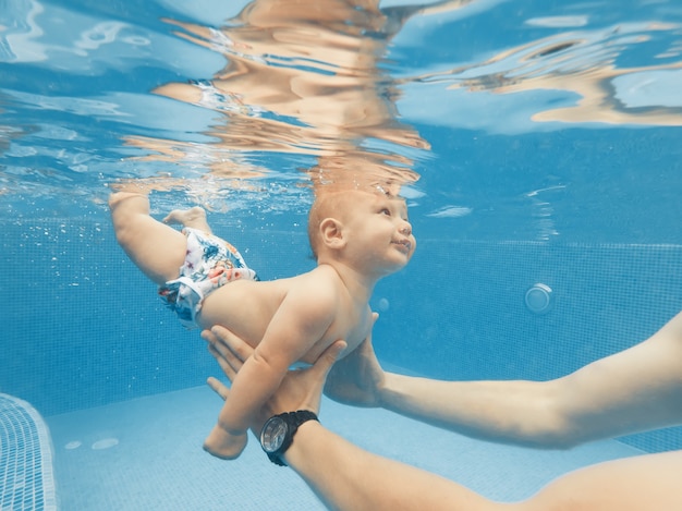 Happy young mother playing with her baby in outdoor swimming pool on a hot summer day. Underwater shooting