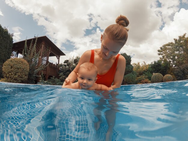 Happy young mother playing with her baby in outdoor swimming pool on a hot summer day