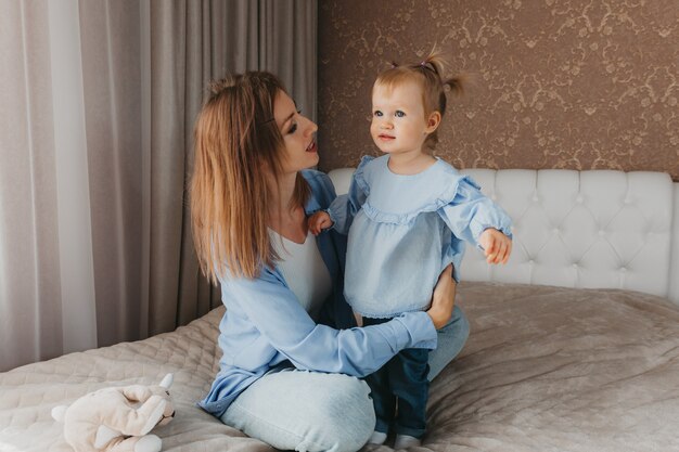 Happy young mother plays with her daughter on the bed at home. mothers Day.