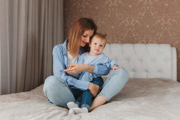 Happy young mother plays with her daughter on the bed at home. mothers Day.