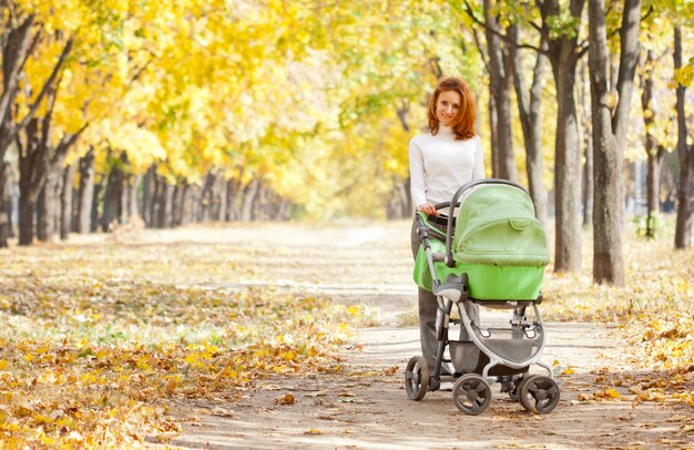 Happy young mother with baby in buggy walking in autumn park