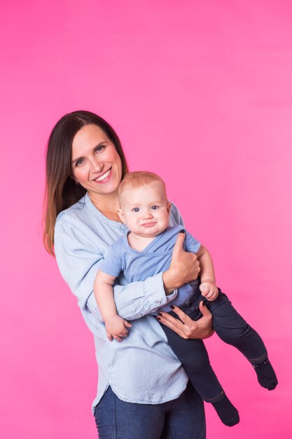 Happy young mother with a baby child on pink wall