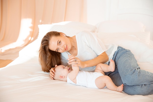 Happy young mother with baby at home in white room mom and baby are lying kissing the baby at home