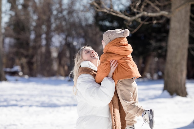 Happy young mother with son walk in the winter park Portrait happy family outdoors Boy throwing snow in mother