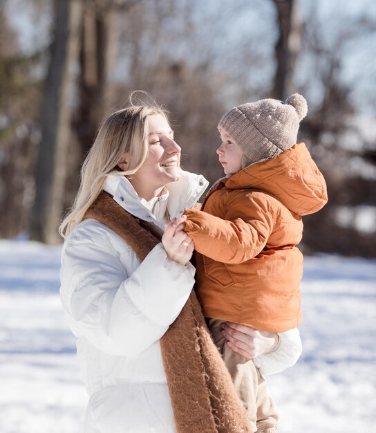 Happy young mother with son walk in the winter park Portrait happy family outdoors Boy throwing snow in mother