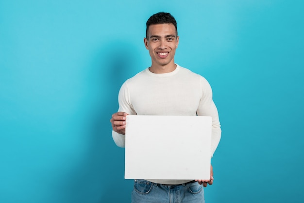 Photo happy young  mulatto man holds in his hands a white blank sheet