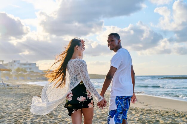 Happy young multi culturial couple running along the beach together