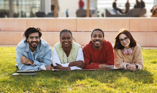 Foto giovani studenti multietnici felici si trovano sull'erba verde riposano nel tempo libero studiano con il dispositivo all'aperto