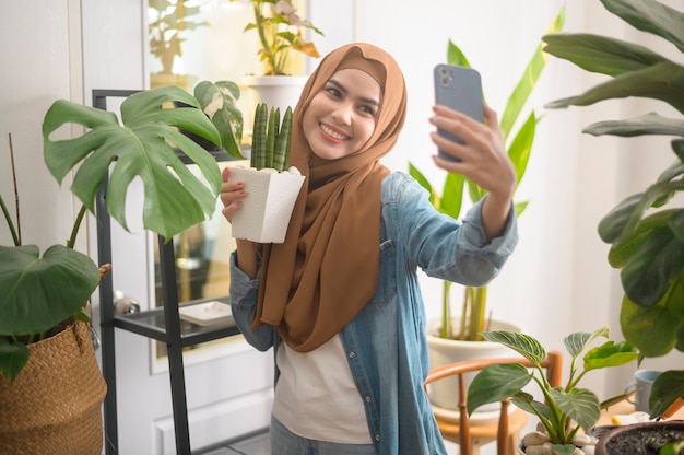 幸せな若いイスラム教徒の女性が植物で自撮りをし、家でビデオ通話をする