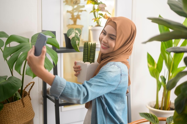 幸せな若いイスラム教徒の女性が植物で自撮りをし、家でビデオ通話をする