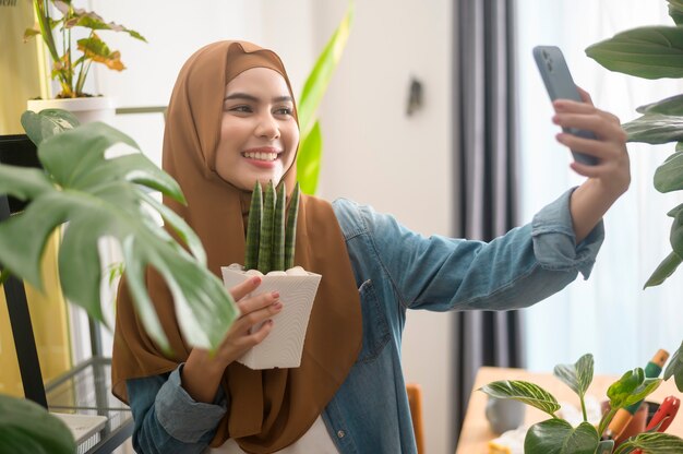 彼女の植物とselfieを取り、自宅でビデオ通話をする幸せな若いイスラム教徒の女性