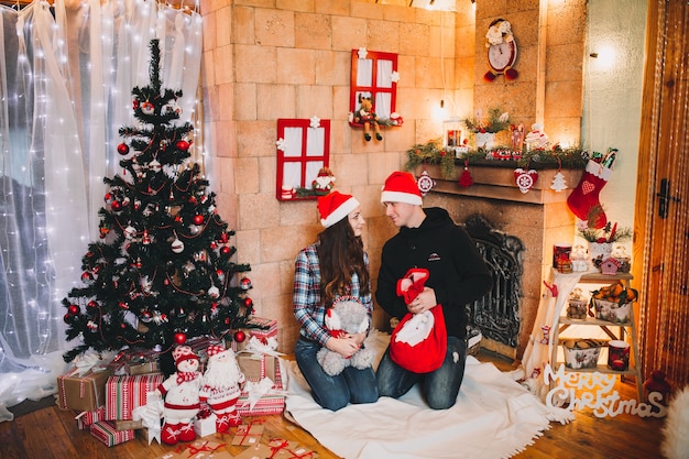 Happy young people by the fireplace near the Christmas tree in Christmas red hat