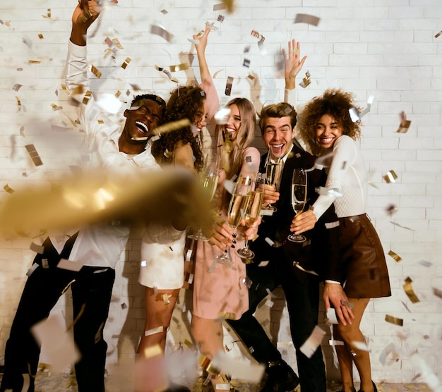 Happy young people celebrating drinking champagne showered with confetti indoor