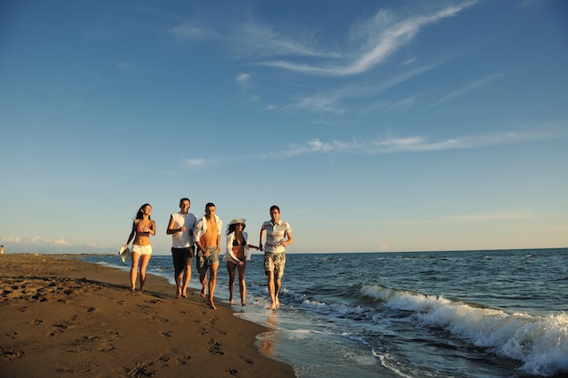 группа счастливых молодых людей весело проводит время, бегая и прыгая на пляже во время заката